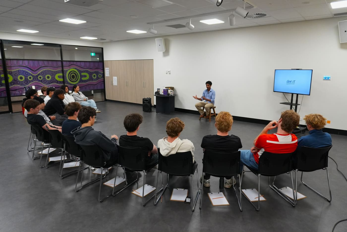 A wide view of young people seated in a semicircle of chairs facing a facilitator
