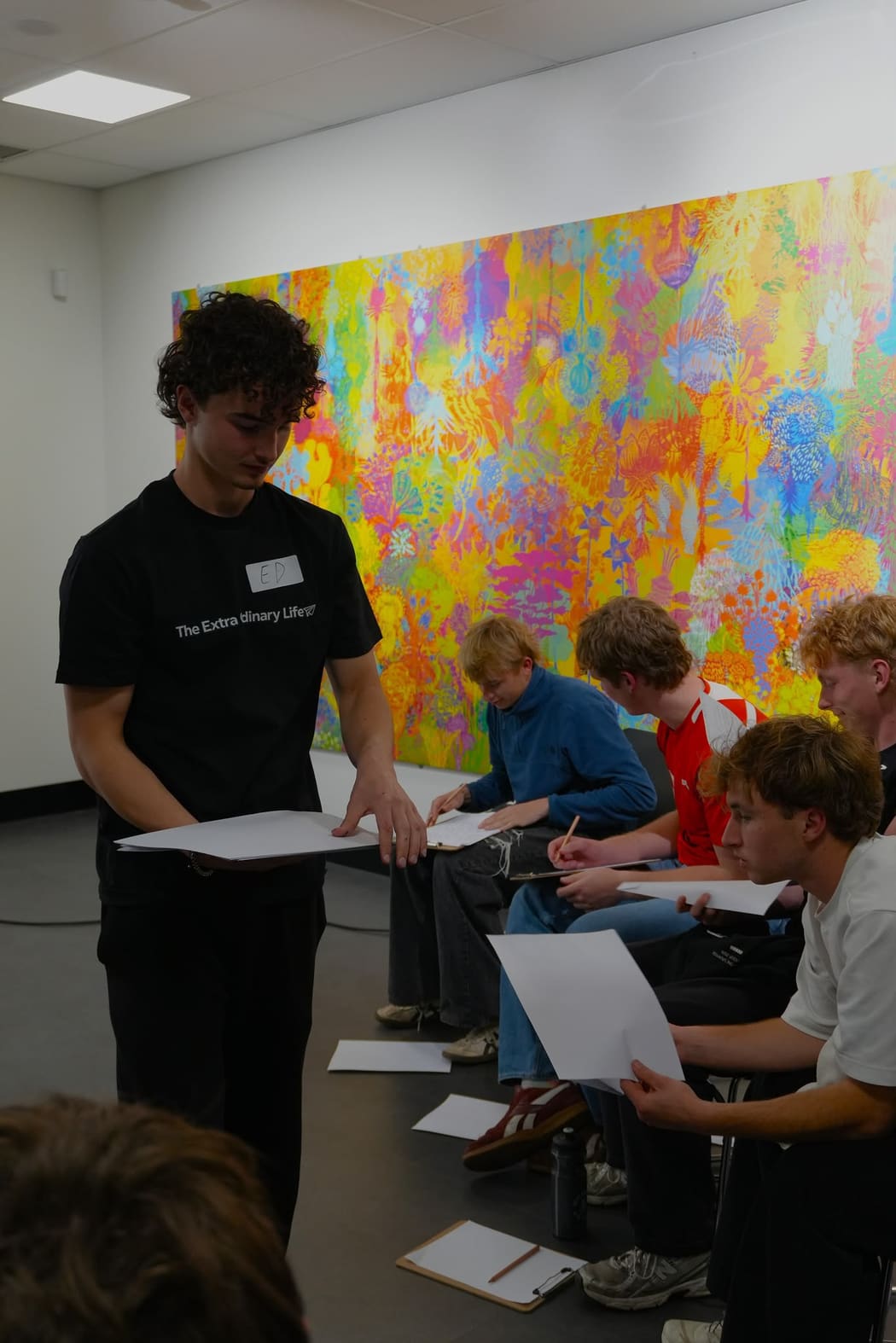 A facilitator in a branded t-shirt handing worksheets to seated participants