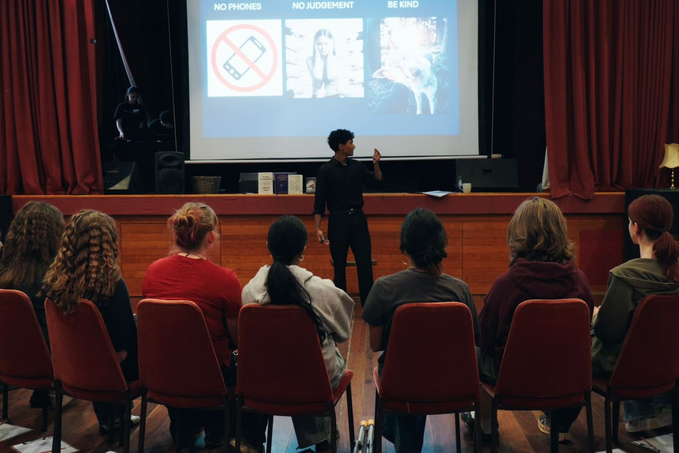 A facilitator standing in front of a projected slide reading No phones, No judgement, Be kind, while participants listen