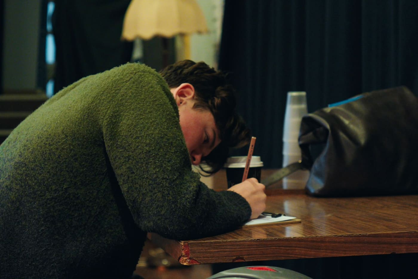 A young person leaning over a table, writing a reflection in pencil
