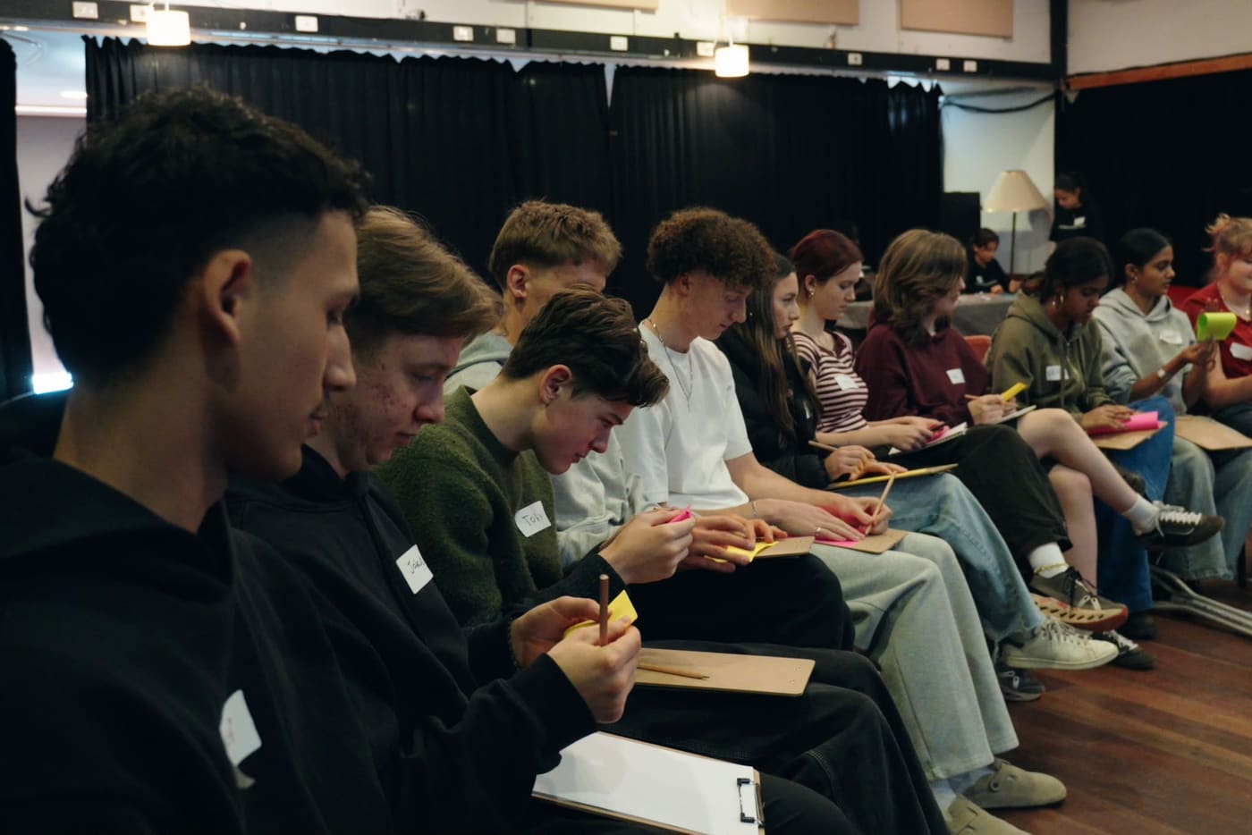 A row of young people writing on clipboards during a reflection exercise